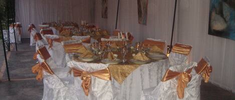 Un salón de banquetes con mesas dispuestas para un evento formal, con manteles blancos y fajas doradas.