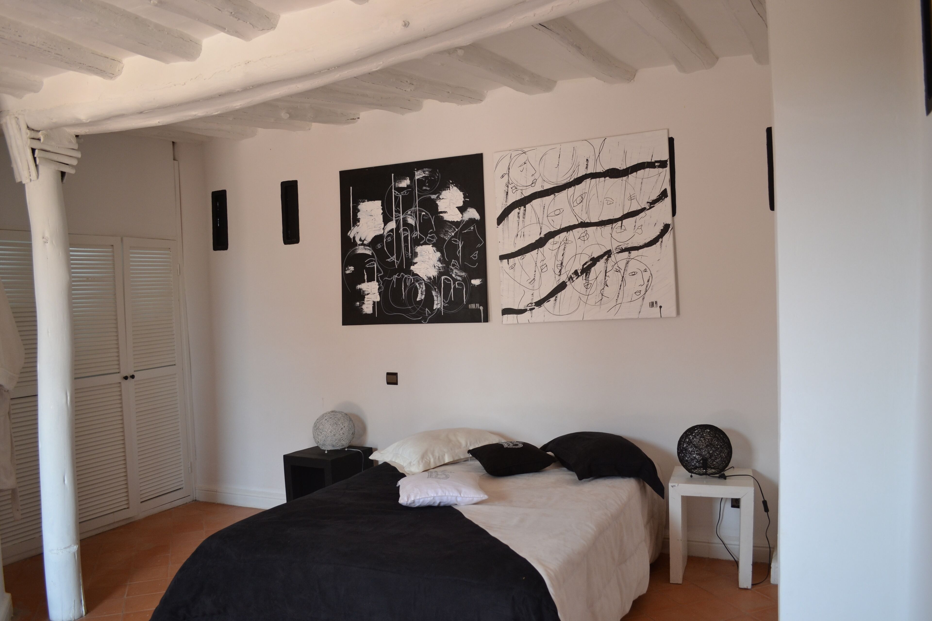 A bedroom with a bed, two wall art pieces, a nightstand, a lamp, and a closet with sliding doors.