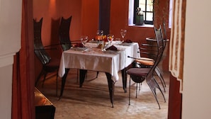 An indoor dining area with a table set for two, a window with a view, and a decorative archway. - Villa Catherine Marrakech (Sidi Abdallah Ghiat)