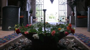 A fountain with roses in a tiled area, surrounded by rocks and potted plants. - Villa Catherine Marrakech (Sidi Abdallah Ghiat)