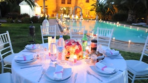 An outdoor dining setup with a pool view, white tablecloths, and candles. - Villa Catherine Marrakech (Sidi Abdallah Ghiat)