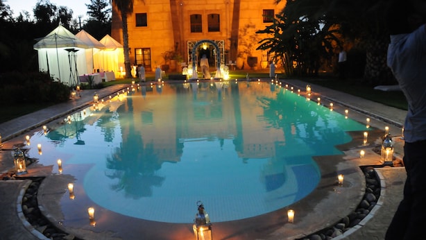 A swimming pool with candles around the edge, a building in the background, and a person standing to the right. - Villa Catherine Marrakech (Sidi Abdallah Ghiat)
