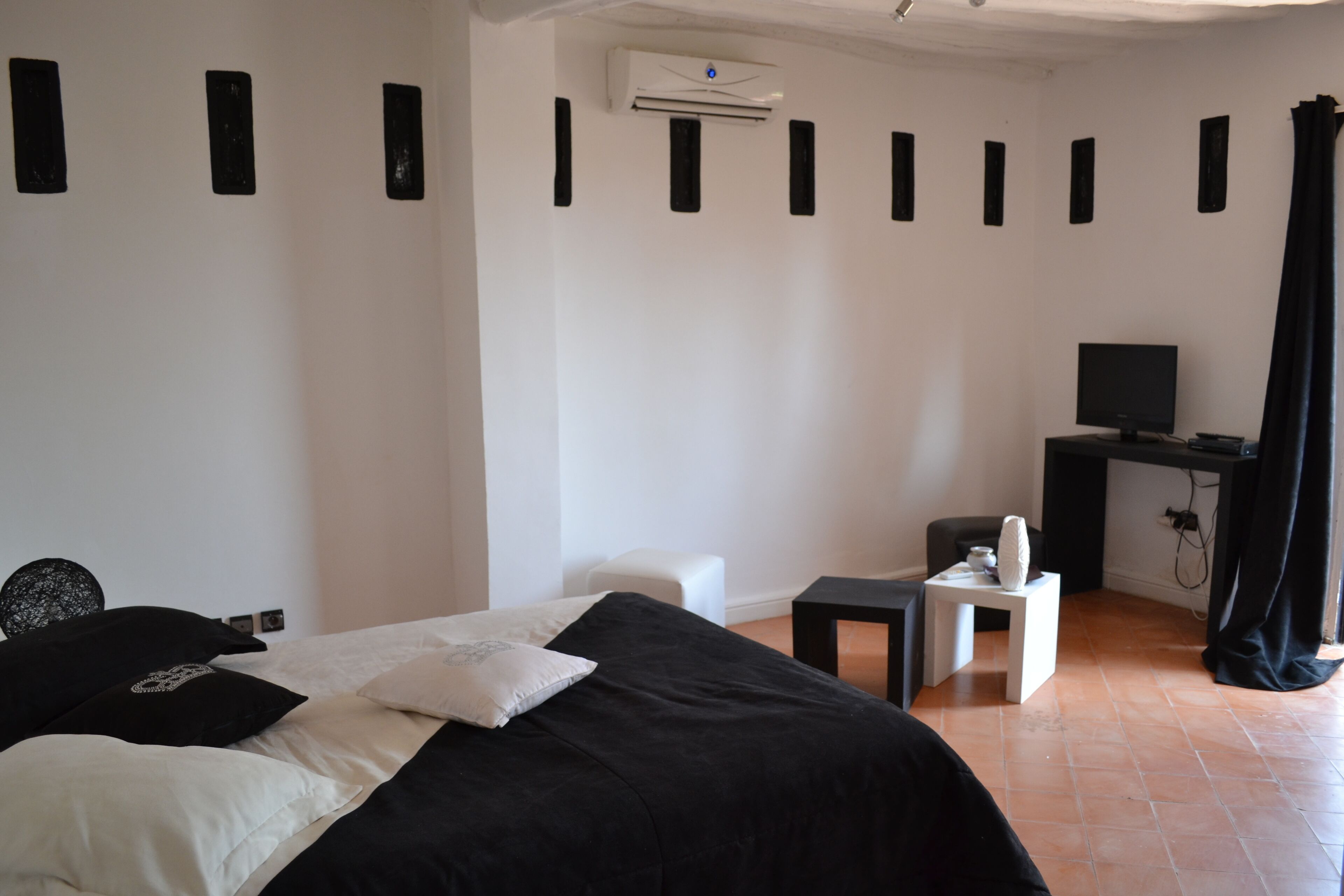 A bedroom with a bed, a desk, a chair, a television, and an air conditioning unit.