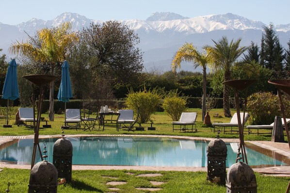 A pool area with lounge chairs and umbrellas, surrounded by greenery and a mountain backdrop.