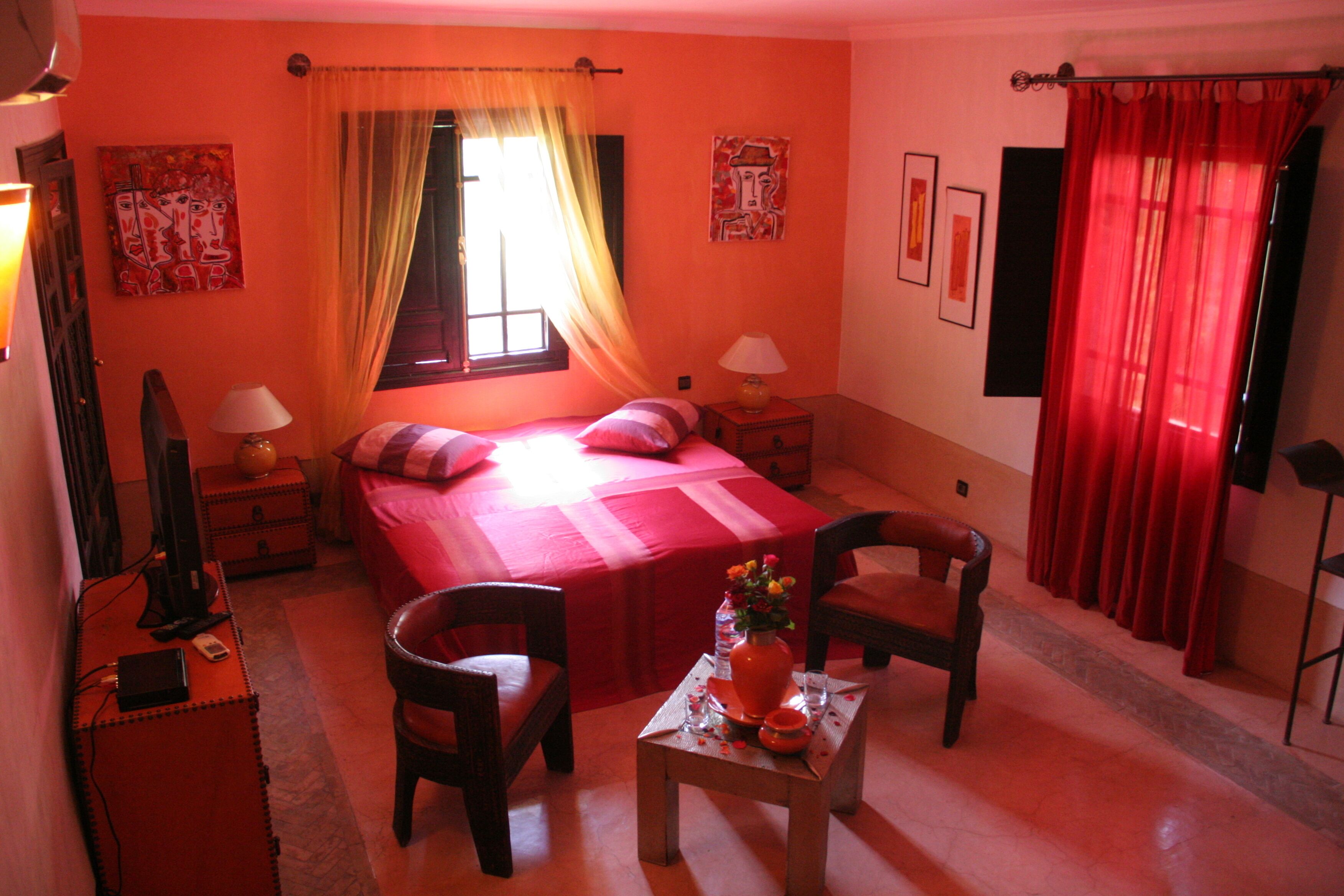 Una habitación con una cama, dos sillas, una mesita con un florero y obras de arte en las paredes.