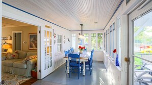 A bright, open-plan living area with a dining table and chairs, a sofa, and a view of a playground through large windows. - The Red Geranium Cottage of Big White Fish Lake! (Pierson Township)