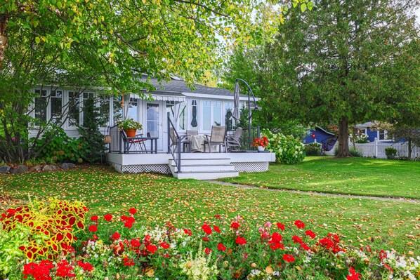 A house with a porch, outdoor seating, and a garden with colorful flowers. - The Red Geranium Cottage of Big White Fish Lake! (Pierson Township)
