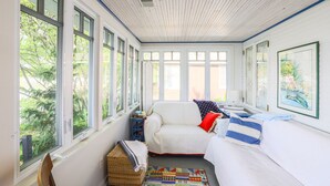 A sunlit room with a white sofa, a small table, and a wicker basket. - The Red Geranium Cottage of Big White Fish Lake! (Pierson Township)
