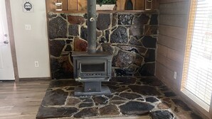 A room with a stone fireplace, wooden walls, and a herringbone-patterned floor. - Large 2Br retro cabin! (Baxter)