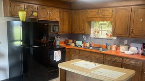 A kitchen with wooden cabinets, a black refrigerator, a wooden island with stools, and a checkered backsplash. - Large 2Br retro cabin! (Baxter)