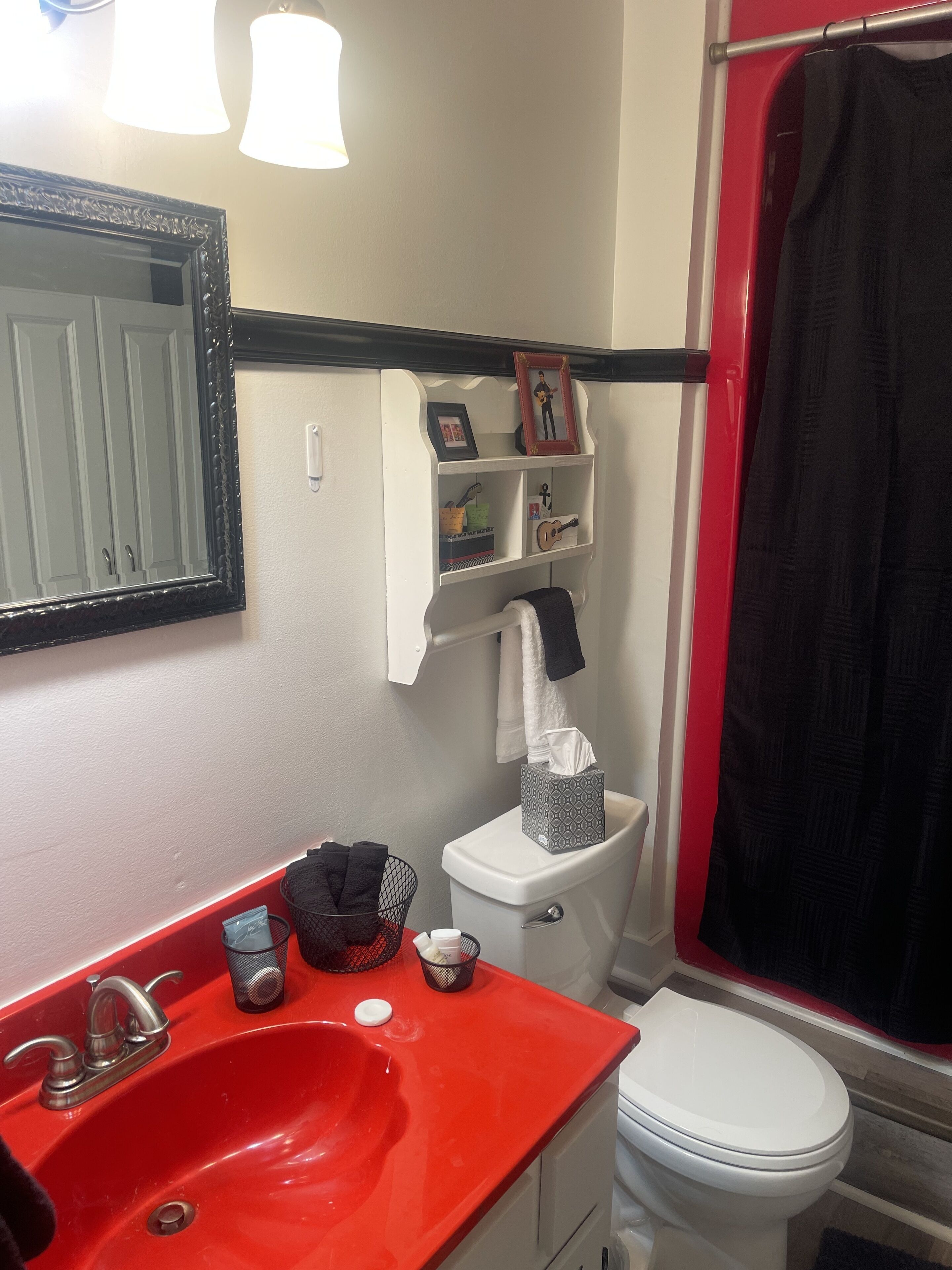 Un baño con un lavamanos rojo, inodoro blanco y cortina de ducha negra.