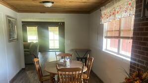 A dining area with a wooden table and chairs, a vase with flowers, and a window with blinds. - Large 2Br retro cabin! (Baxter)