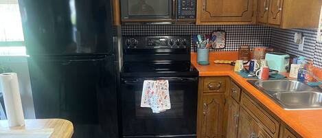 A kitchen with wooden cabinets, a black refrigerator, a microwave, and a stove.