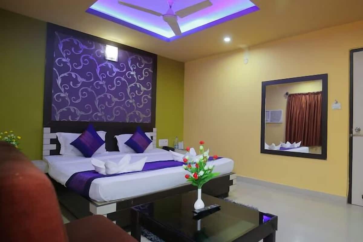 Ein Hotelzimmer mit einem Bett, einem Nachttisch mit Blumenvase, einem Deckenventilator und einem Spiegel an der Wand.