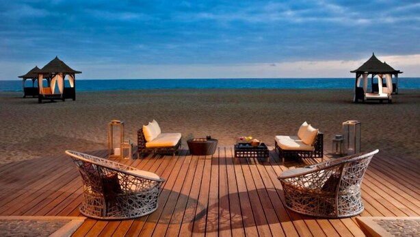 A wooden deck with wicker chairs and a table, two gazebos, and a beach view. - VILLA TORTUGA BEACH RESORT (Sal)