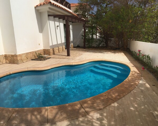 A swimming pool with a stone border, a pergola, and a white building with a tiled roof. - VILLA TORTUGA BEACH RESORT (Sal)