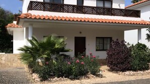 A two-story house with a tiled roof, a balcony with a lattice design, and a front garden with various plants and flowers. - VILLA TORTUGA BEACH RESORT (Sal)