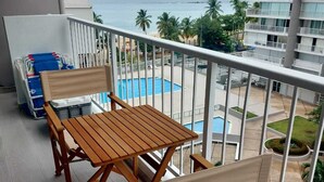 Ein Balkon mit Holztisch und -stühlen, der auf einen Swimmingpool und ein Gebäude mit mehreren Balkonen blickt.