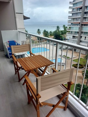 Un balcón con una mesa y sillas de madera, con vistas a una piscina y un edificio con varios balcones.
