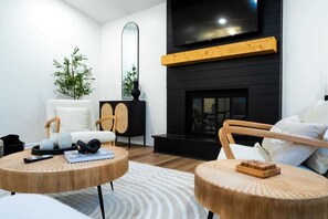 A modern living room with a fireplace, round wooden tables, a sofa, and a TV mounted on the wall.