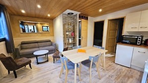 Uma sala de estar aconchegante com um sofá, uma mesinha redonda e uma mesa de jantar com cadeiras. Há uma cozinha com micro-ondas e um refrigerador pequeno.