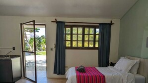 A hotel room with two beds, a ceiling fan, a window with curtains, and a view of greenery outside.