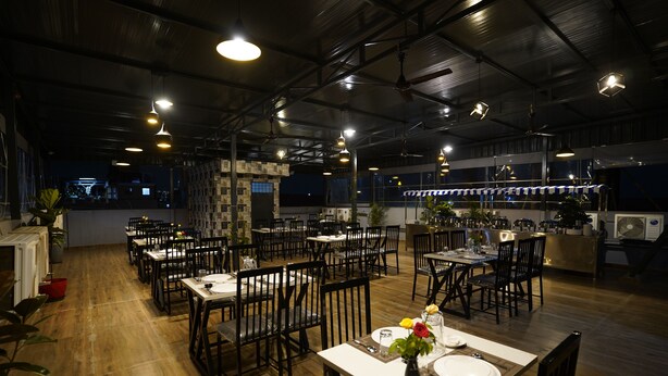 A restaurant with multiple tables and chairs, wooden flooring, and pendant lighting. - Sai Bliss International, Manyata Tech Park (Bengaluru)