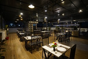 A restaurant with multiple tables and chairs, wooden flooring, and pendant lighting. - Sai Bliss International, Manyata Tech Park (Bengaluru)