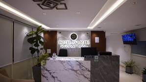 A hotel reception desk with a marble top, a large potted plant, and a digital screen displaying a slideshow. - Sai Bliss International, Manyata Tech Park (Bengaluru)