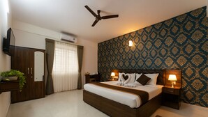 A bedroom with a bed, bedside tables, a ceiling fan, an air conditioning unit, a wardrobe, and a patterned wall. - Sai Bliss International, Manyata Tech Park (Bengaluru)