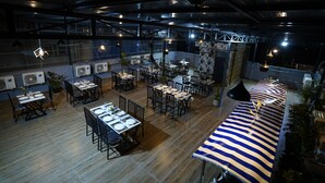 A spacious restaurant with multiple tables and chairs, air conditioning units, and hanging pendant lights. - Sai Bliss International, Manyata Tech Park (Bengaluru)