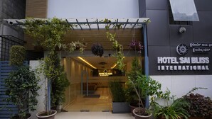 The entrance of Hotel Sai Bliss International with a modern design, featuring a glass door, potted plants, and a signboard. - Sai Bliss International, Manyata Tech Park (Bengaluru)
