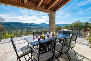 Une terrasse extérieure avec une table et des chaises, un pilier en pierre et une vue sur les montagnes.