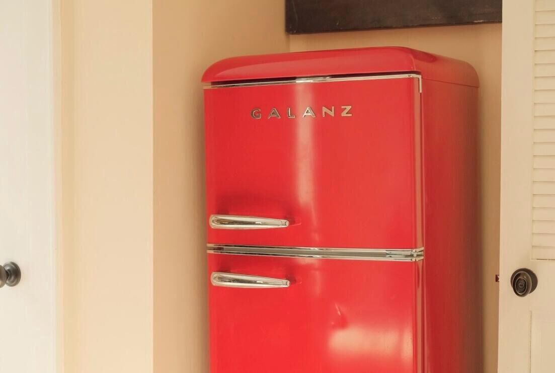 A red vintage refrigerator with the brand name 'GALANZ' on it, located in a room with beige walls.