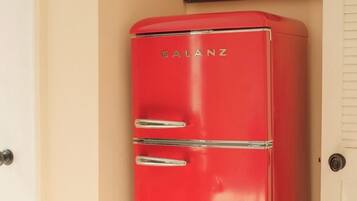 A red vintage refrigerator with the brand name 'GALANZ' on it, located in a room with beige walls.