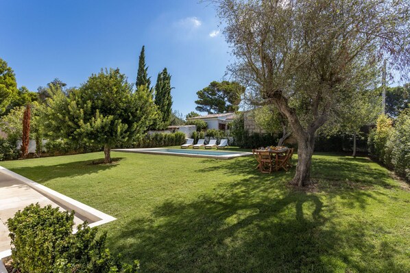 A well-maintained garden with a swimming pool, lounge chairs, and a dining area.