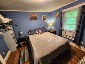 A bedroom with a bed, a nightstand, a lamp, a window with curtains, and wall art.