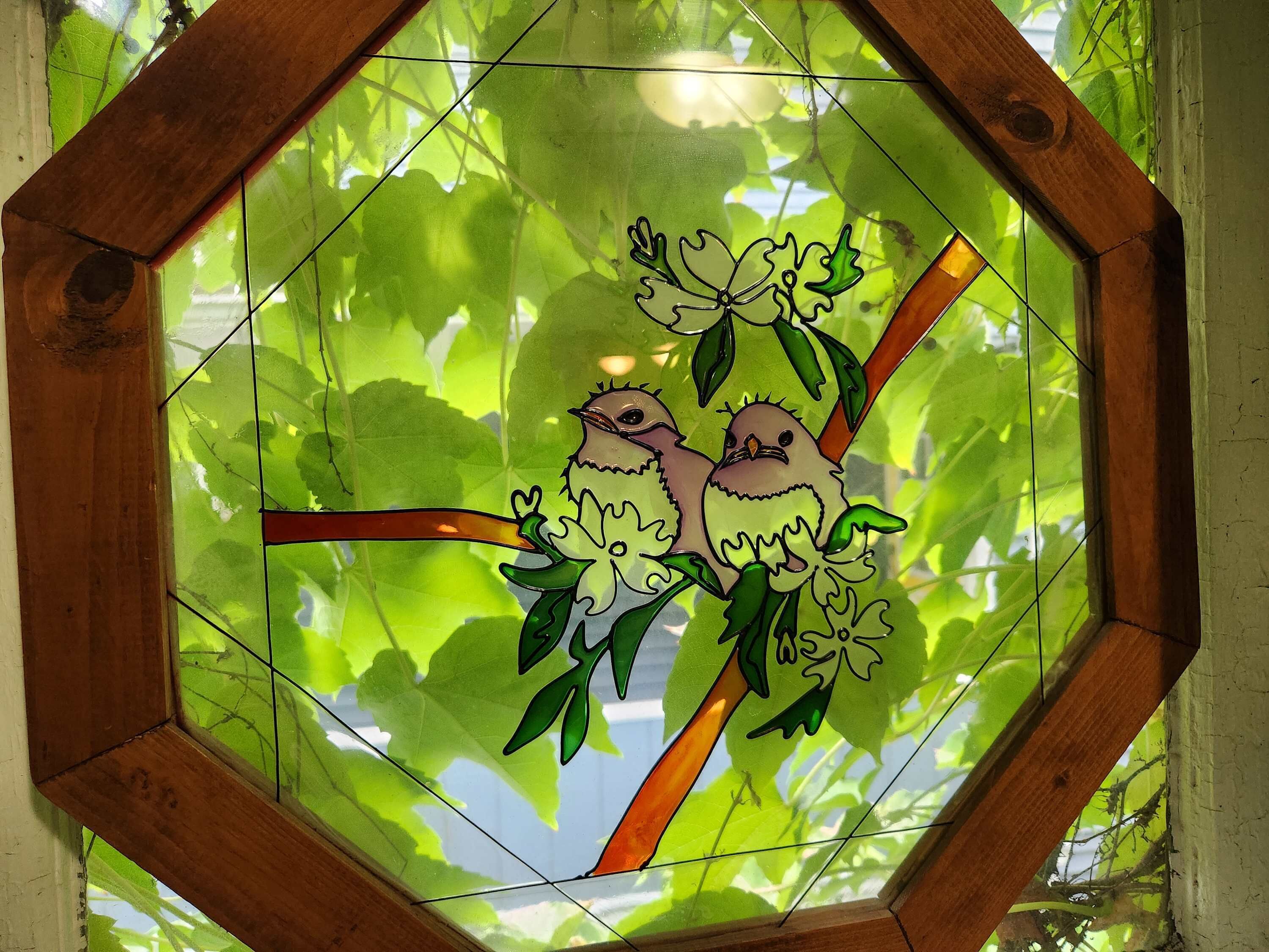 A stained glass window with a geometric frame, depicting two birds on a branch.