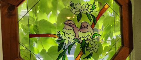 A stained glass window with a geometric frame, depicting two birds on a branch.