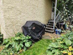 Un barbecue abrité, une poubelle et un escalier menant à une porte.