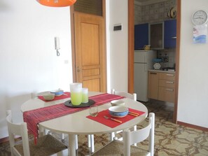 A dining area with a round table, chairs, and a kitchen in the background. - Spacious Flat Near Pluto Beach (San Michele al Tagliamento)