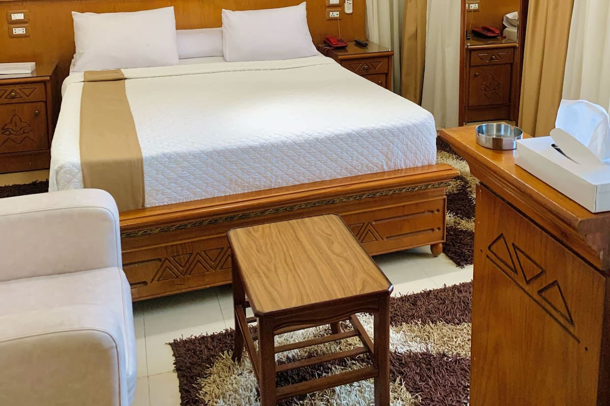A hotel room with a large bed, wooden headboard, two bedside tables, a nightstand, a wooden dresser, a mirror, and a small wooden table.