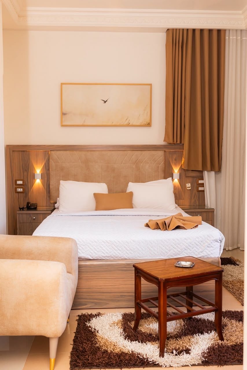 Una habitación de hotel con una cama grande, mesitas de noche, una pequeña mesa de madera y un cuadro en la pared.