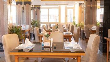 A hotel dining area with tables and chairs, decorative ceiling, and large windows.