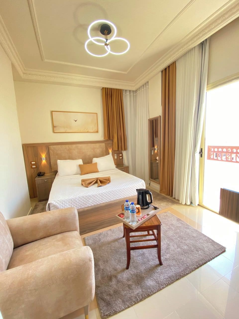 Hotelkamer met een bed, bureau, stoel, koffiezetapparaat en een groot raam met gordijnen.