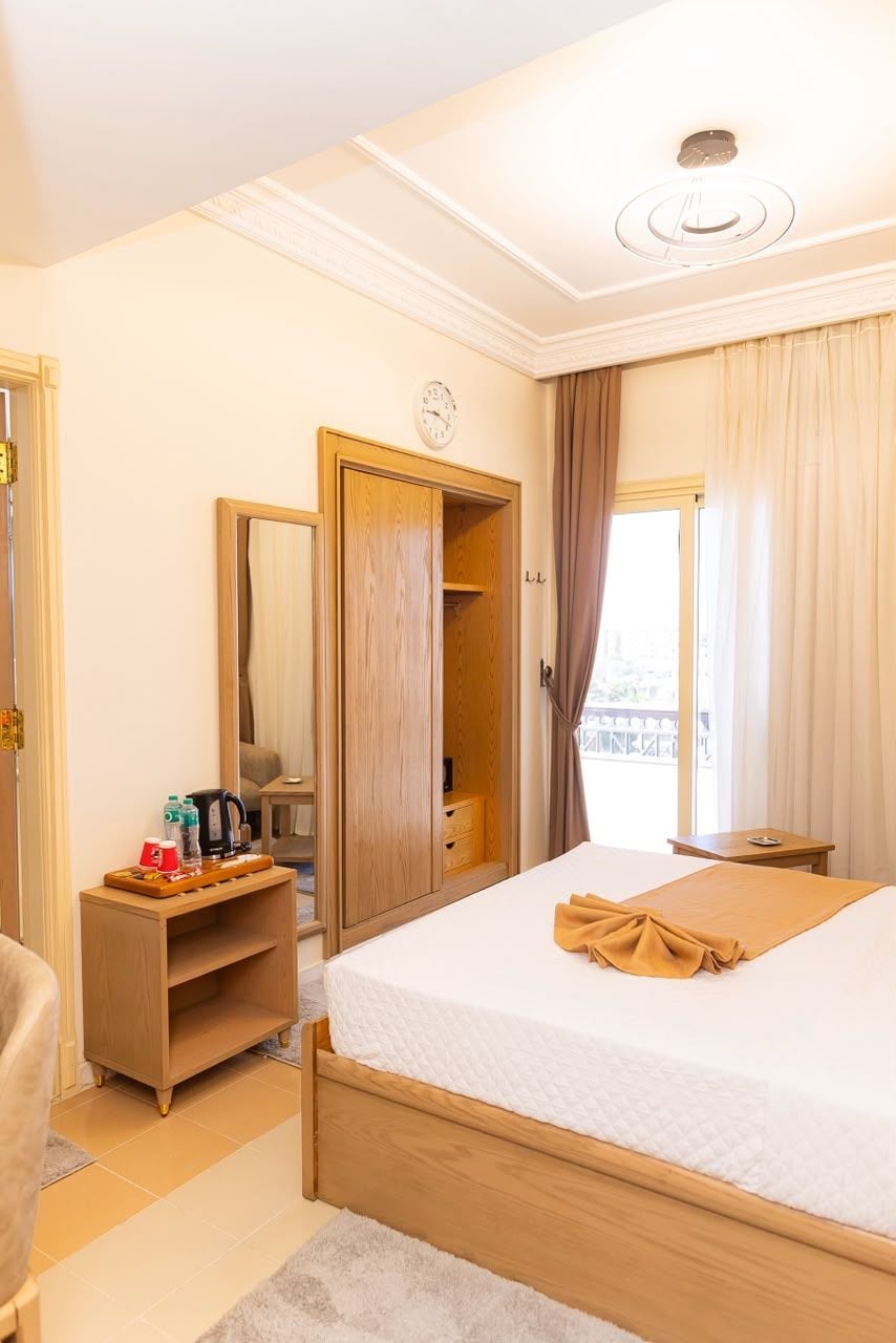 Une chambre d’hôtel avec un lit, une table de chevet, un miroir, une armoire et une fenêtre avec des rideaux.
