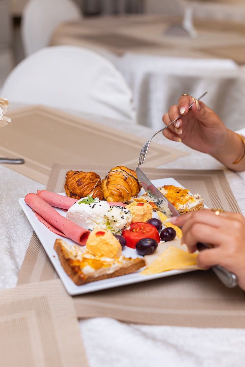 Bandeja de desayuno con cruasanes, jamón, queso, tomates y un sándwich croque-monsieur sobre una cama.