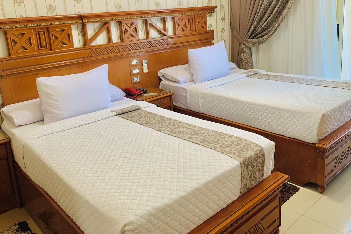 Two double beds with wooden headboards, white bedding, and a bedside table with a phone and remote control.