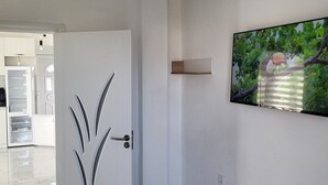 Un interior moderno con una puerta blanca, un banco de madera, un televisor montado y un suelo de mármol.