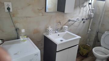 A bathroom with a white sink, a mirror, a toilet, and a washing machine.